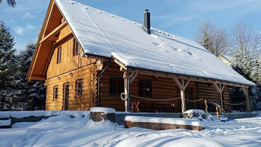 Roubenka pod sněhem za slunečného zimního dne, kolem zasněžené smrky