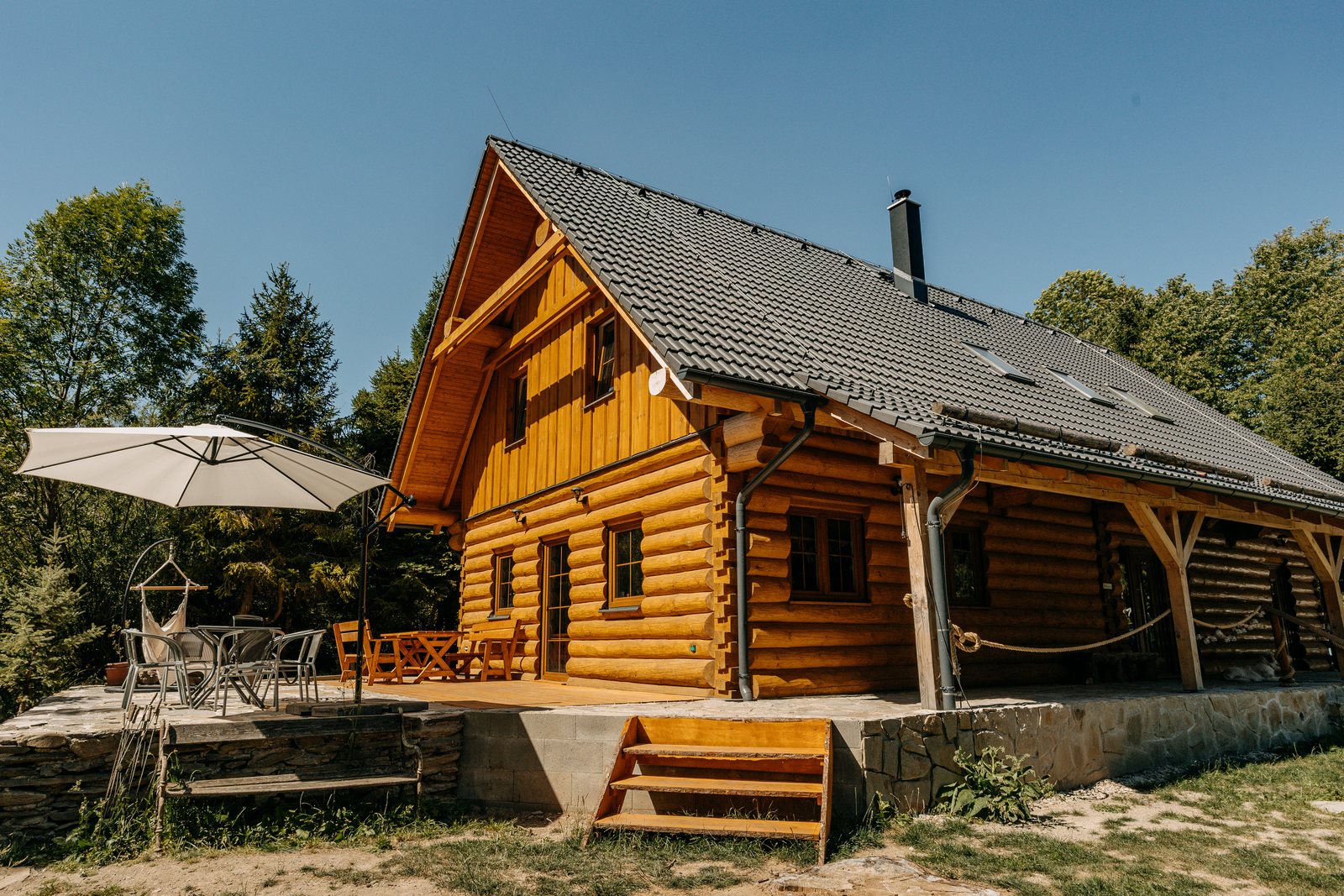 Dřevěná roubenka Chata u Lubátka s krytou terasou a slunečníkem za letního dne