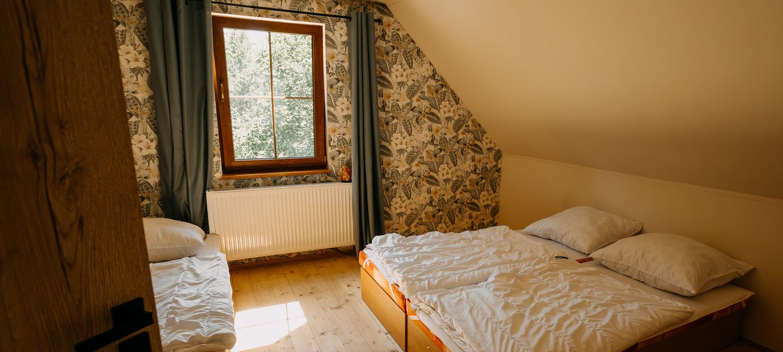 Podkrovní ložnice s manželskou postelí, zelenými závěsy a připraveným povlečením
